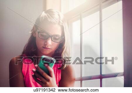 Young girl wearing glasses, beside window, using smartphone View Large Photo Image Stock Image - Young girl wearing glasses, beside window, using smartphone. Fotosearch