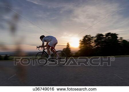 Young male cyclist cycling down rural road at sunset View Large Photo Image Stock Photograph - Young male cyclist cycling down rural road at sunset. Fotosearch