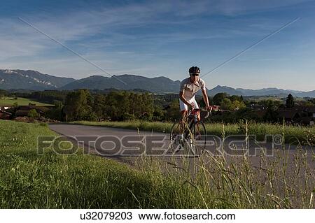 Stock Image - Young male cyclist cycling up rural road. Fotosearch
