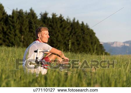 Stock Photo - Young male cyclist sitting in field looking out. Fotosearch