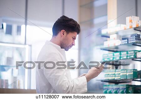 Young male pharmacist reading medical drug packet in pharmacy View Large Photo Image Stock Photo - Young male pharmacist reading medical drug packet in pharmacy. Fotosearch
