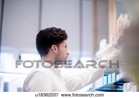 Young male pharmacist removing medical drug from pharmacy shelves View Large Photo Image Stock Photo - Young male pharmacist removing medical drug from pharmacy shelves. Fotosearch
