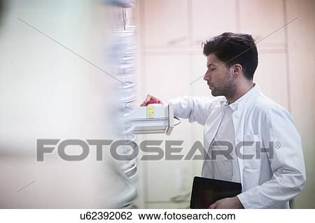 Stock Image - Young male pharmacist removing pill bottle from pharmacy drawer. Fotosearch