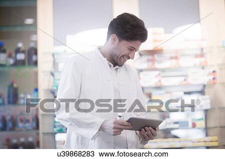 Stock Image - Young male pharmacist using digital tablet in pharmacy. Fotosearch