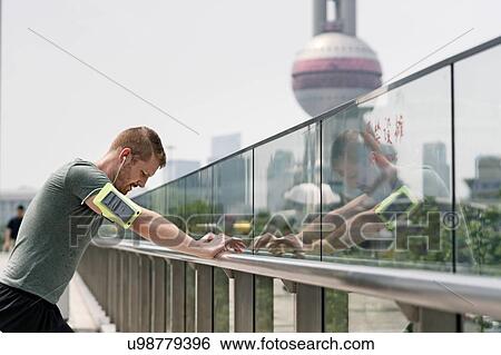 Stock Photograph - Young male runner leaning against handrail in Shanghai financial centre, Shanghai, China. Fotosearch
