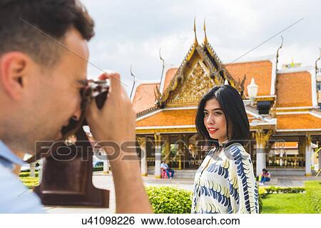 Young male tourist photographing girlfriend outside temple, Bangkok, Thailand View Large Photo Image Stock Photograph - Young male tourist photographing girlfriend outside temple, Bangkok, Thailand. Fotosearch