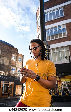 Young man outdoors, wearing earphones, using smartphone View Large Photo Image Stock Image - Young man outdoors, wearing earphones, using smartphone. Fotosearch