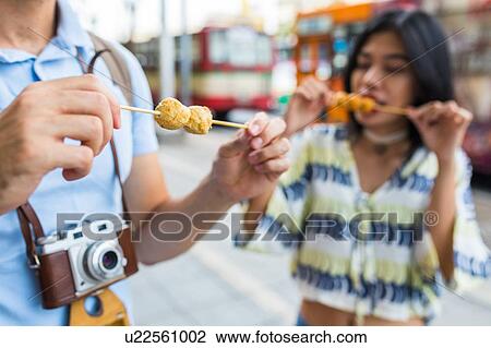 Young tourist couple eating skewered street food on sidewalk, Bangkok, Thailand View Large Photo Image Stock Image - Young tourist couple eating skewered street food on sidewalk, Bangkok, Thailand. Fotosearch
