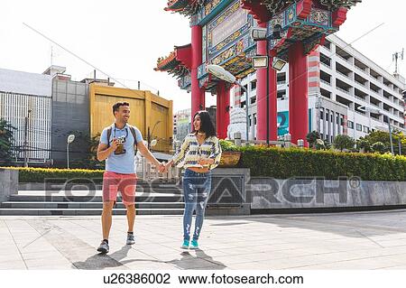 Stock Image - Young tourist couple walking on sidewalk, Bangkok, Thailand. Fotosearch