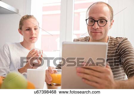 Young woman and boyfriend looking at digital tablet at breakfast table View Large Photo Image Stock Photo - Young woman and boyfriend looking at digital tablet at breakfast table. Fotosearch
