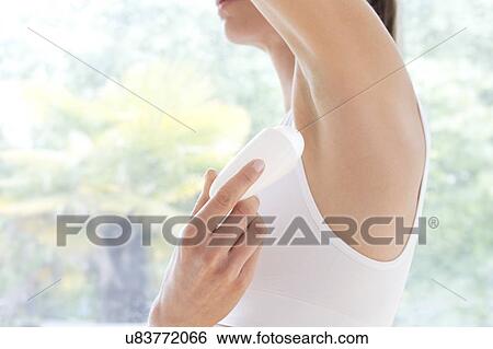 Stock Photograph - Young woman applying underarm deodorant, close up.. Fotosearch