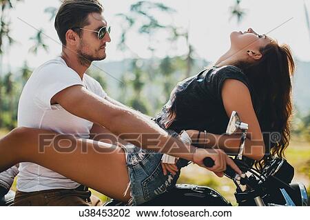 Stock Image - Young woman astride boyfriend on motorcycle, Krabi, Thailand. Fotosearch