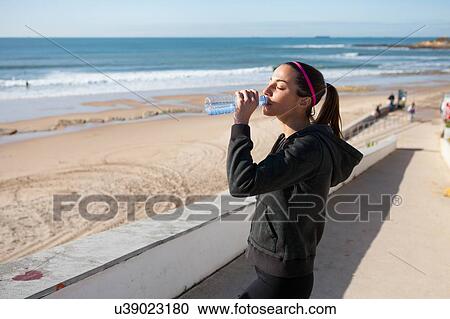 Stock Image - Young woman at beach drinking water from water bottle, Carcavelos, Lisboa, Portugal, Europe. Fotosearch
