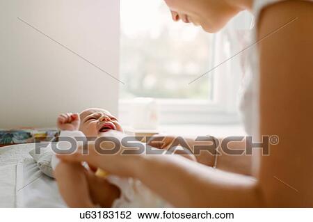 Young woman changing baby daughter's diaper on bed View Large Photo Image Stock Image - Young woman changing baby daughter's diaper on bed. Fotosearch