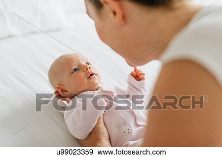 Young woman cradling baby daughter on bed, over shoulder view View Large Photo Image Stock Photo - Young woman cradling baby daughter on bed, over shoulder view. Fotosearch