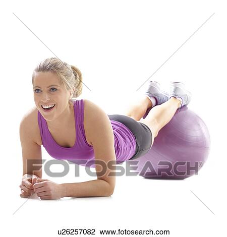 Stock Image - Young woman doing plank on fitness ball, studio shot.. Fotosearch