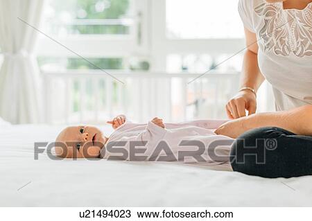 Young woman dressing baby daughter on bed, cropped View Large Photo Image Stock Image - Young woman dressing baby daughter on bed, cropped. Fotosearch