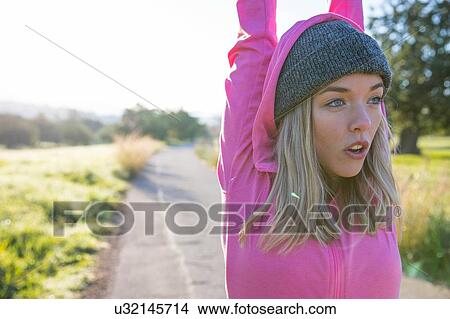 Picture - Young woman exercising in rural setting, stretching, arms raised. Fotosearch