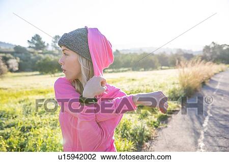 Stock Image - Young woman exercising in rural setting, stretching arm. Fotosearch