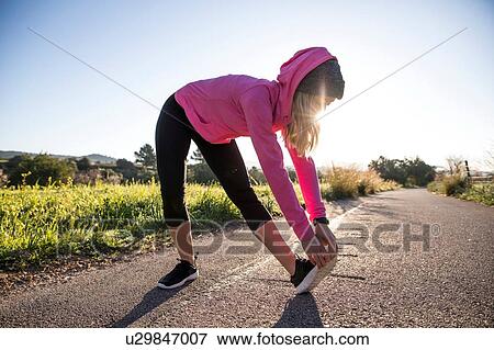 Stock Photo - Young woman exercising in rural setting, stretching. Fotosearch