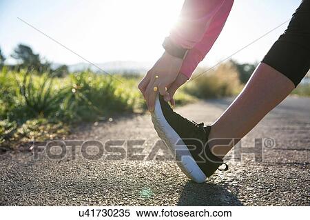 Stock Photography - Young woman exercising in rural setting, stretching leg, low section. Fotosearch