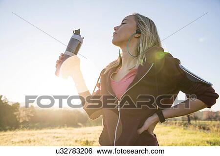 Stock Photograph - Young woman exercising outdoors, holding water bottle. Fotosearch