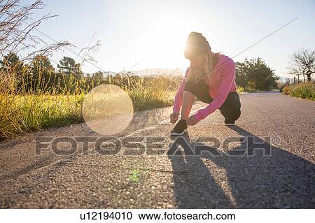 Stock Image - Young woman exercising outdoors, tying shoelace. Fotosearch