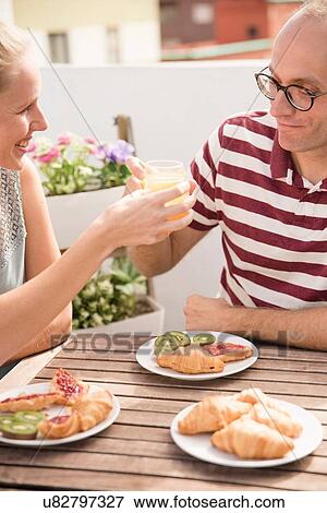 Stock Photo - Young woman handing breakfast orange juice to boyfriend at patio table. Fotosearch