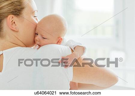 Stock Image - Young woman holding baby daughter, over shoulder view. Fotosearch