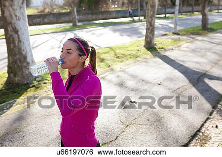 Stock Photograph - Young woman in street drinking water from water bottle. Fotosearch