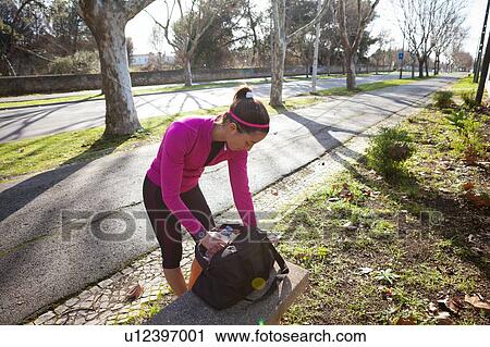 Stock Image - Young woman in street searching through backpack. Fotosearch