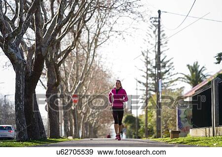 Stock Photo - Young woman jogging in tree lined street. Fotosearch
