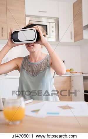 Young woman looking through virtual reality headset at kitchen table View Large Photo Image Stock Image - Young woman looking through virtual reality headset at kitchen table. Fotosearch