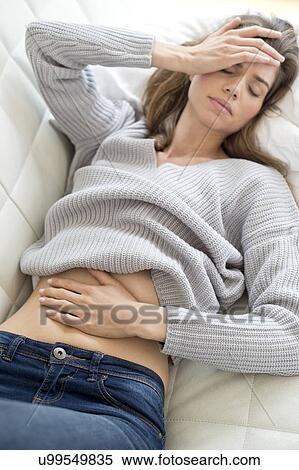 Young woman lying down with hand on stomach and head. View Large Photo Image Stock Photography - Young woman lying down with hand on stomach and head.. Fotosearch