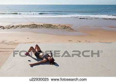 Stock Photography - Young woman lying on back by beach, Carcavelos, Lisboa, Portugal, Europe. Fotosearch