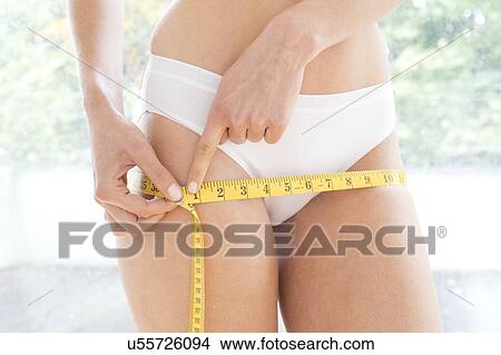 Young woman measuring her hips with a tape measure. View Large Photo Image Picture - Young woman measuring her hips with a tape measure.. Fotosearch