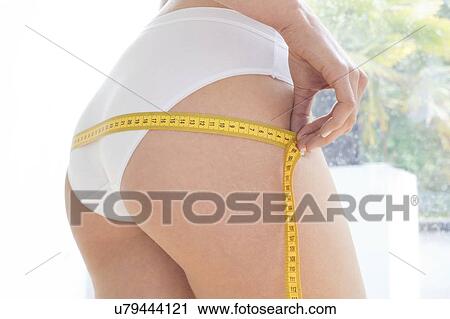 Stock Image - Young woman measuring her hips with a tape measure.. Fotosearch
