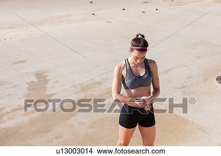 Picture - Young woman on beach looking at fitness tracker, Carcavelos, Lisboa, Portugal, Europe. Fotosearch