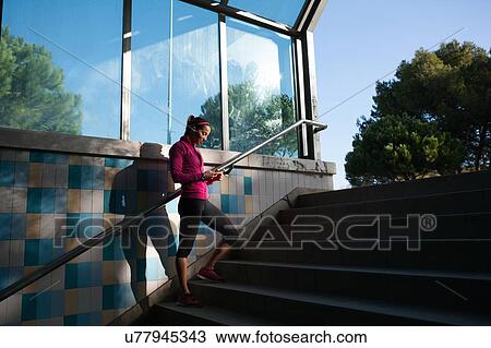 Stock Image - Young woman on stairway texting on smartphone. Fotosearch