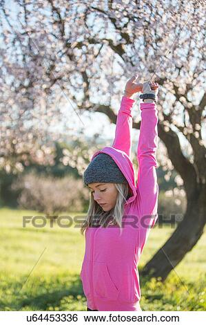 Stock Photograph - Young woman outdoors, exercising, stretching, arms raised. Fotosearch