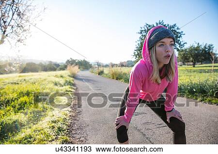 Stock Image - Young woman outdoors, taking a break from exercising, hands on knees. Fotosearch