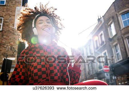Stock Image - Young woman, outdoors, wearing headphone, smiling. Fotosearch