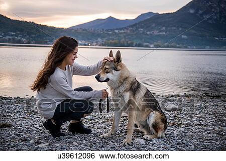 Stock Photograph - Young woman petting dog on riverbank, Vercurago, Lombardy, Italy. Fotosearch