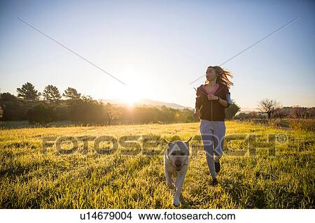 Young woman running across field, with pet dog View Large Photo Image Picture - Young woman running across field, with pet dog. Fotosearch