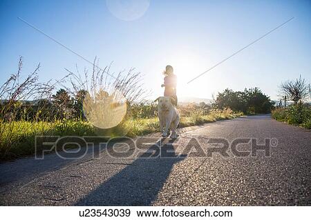 Young woman running along rural road with pet dog, low angle view View Large Photo Image Stock Photo - Young woman running along rural road with pet dog, low angle view. Fotosearch