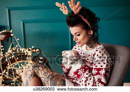 Young woman sitting at home, wearing christmas jumper and antlers, drinking hot drink View Large Photo Image Stock Image - Young woman sitting at home, wearing christmas jumper and antlers, drinking hot drink. Fotosearch