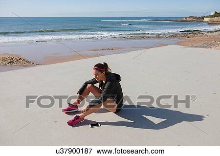 Stock Photo - Young woman sitting by beach, Carcavelos, Lisboa, Portugal, Europe. Fotosearch