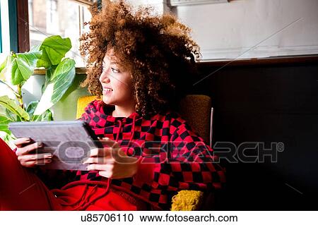 Stock Image - Young woman sitting indoors, using digital tablet. Fotosearch