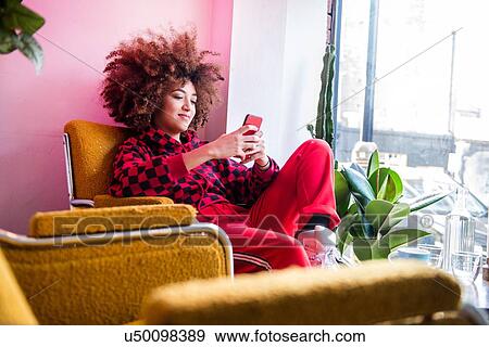 Stock Photo - Young woman sitting indoors, using smartphone. Fotosearch