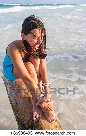 Stock Image - Young woman sitting on log above sea, Tulum, Quintana Roo, Mexico. Fotosearch